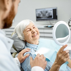 Dental implant patient admiring her new smile in a mirror