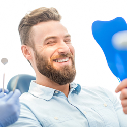 Bearded man with porcelain veneers happily looking at a mirror