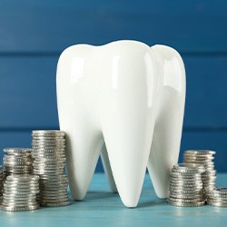 A ceramic tooth model and coins on a light blue table