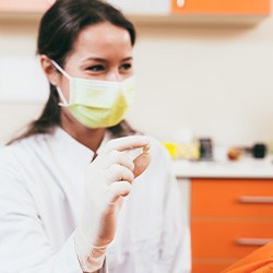Dentist in white coat holding model tooth in one hand and blue piggy bank in the other
