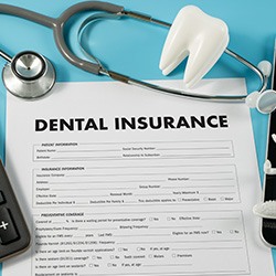 Dental insurance form on light blue surface next to calculator and dental devices