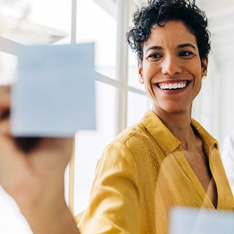 Woman in yellow shirt smiling while writing on post-it