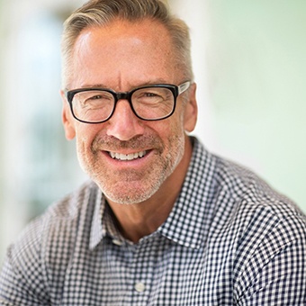 A middle-aged man wearing glasses and a plaid shirt and smiling after seeing his Delta Dental dentist in McKinney