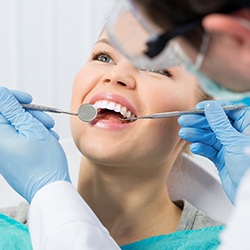 A young female patient smiling while a dentist checks her teeth and gums during a checkup