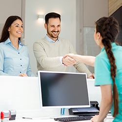 A man and woman shaking hands with the dental receptionist upon their arrival