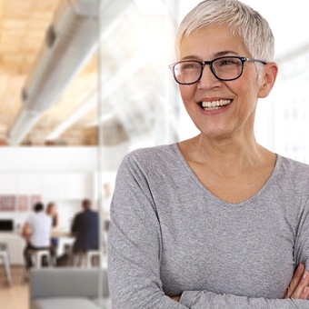 An older woman standing inside a business with her arms crossed and smiling after using her Humana dental insurance in McKinney to take care of her smile