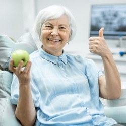 A senior woman holding an apple while in a dentist’s office