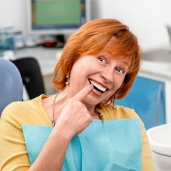: A woman pointing to her new dental implant in a dentist’s office