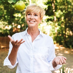 Woman smiling outside while tossing a green apple in the air