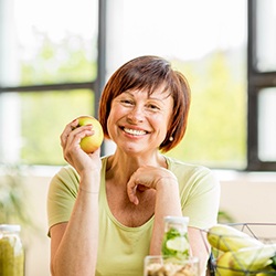Happy woman holding an apple after dental implant tooth replacement