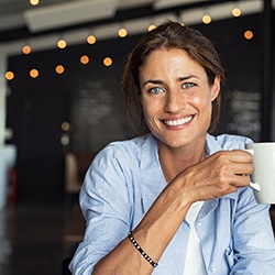 Smiling woman holding a white mug after dental implant tooth replacement
