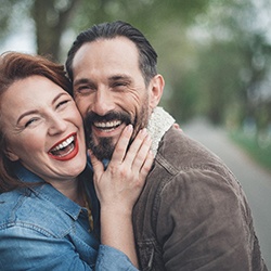 Couple laughing together in a park after dental implant tooth replacement
