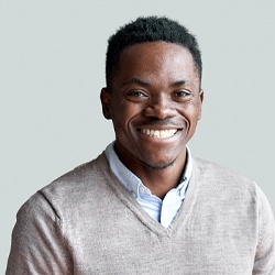 A young man wearing a gray sweater smiles after completing his Invisalign treatment