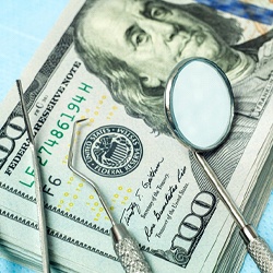 A stack of money with dental instruments lying on top of it