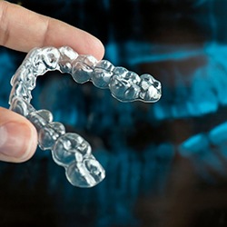 Hand holding an Invisalign aligner tray in front of dental x-ray
