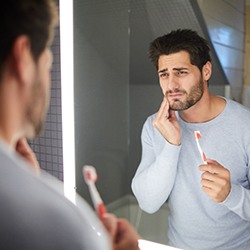 Man holding toothbrush touching his cheek in pain because of gum disease
