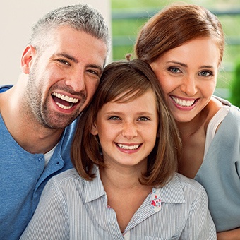 Family of three smiling after preventive dentistry