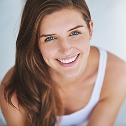 Lady in white tank top smiling after dental checkup and teeth cleaning