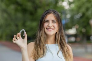 Smiling woman holding Invisalign aligners while outside