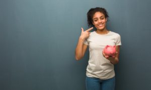 woman holding a pink piggy bank and pointing to her smile 