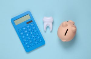 Birds eye view of a piggy bank, model tooth, and blue basic calculator on a light blue background