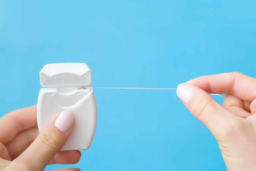 Manicured fingers pulling string floss out of white container with blue background